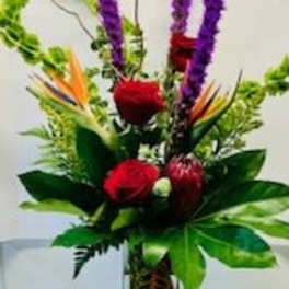 Tropical flower arrangement with red roses and purple spikes in a glass vase