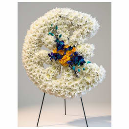 Large white floral wreath on a black stand with a small yellow and blue center cluster