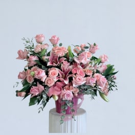 Pink roses and lilies arranged in a pink vase with ribbon