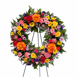 Colorful floral wreath on a black stand with roses and daisies