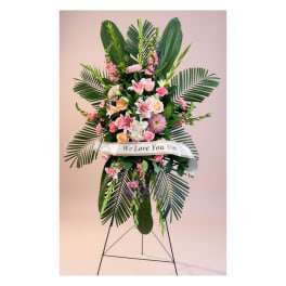 Tall pink and white floral standing spray with a ribbon on a metal easel