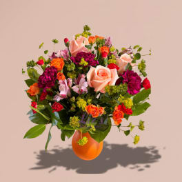 Mixed bouquet of roses, carnations, and alstroemeria in an orange vase