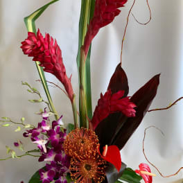 Tropical floral arrangement with red ginger, purple orchids, and anthuriums in a black vase