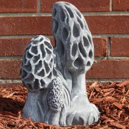 Gray mushroom-shaped garden sculpture beside a brick wall