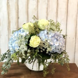 Blue and lavender hydrangeas with pale yellow roses in a glass vase