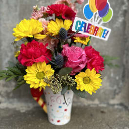 Bright mixed bouquet in a decorated vase with a colorful "Celebrate!" topper