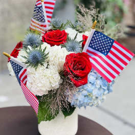 Red roses and hydrangeas in a white vase with small American flags