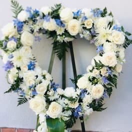 Heart-shaped floral wreath with white roses and blue flowers on an easel