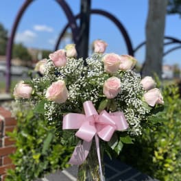 Pink roses and baby's breath in a clear glass vase with a pink ribbon
