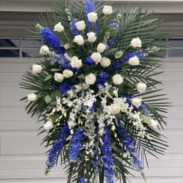 Tall standing floral spray with white roses, blue delphinium, and white orchids