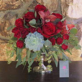 Red roses and orchids arranged in a silver vase with a blue succulent accent