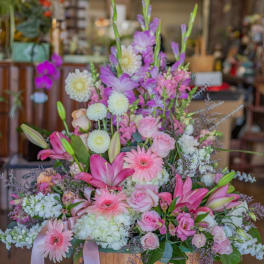 Large pastel flower arrangement with pink lilies, roses, and gerbera daisies in a wooden basket