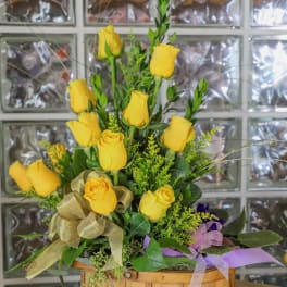 Yellow roses arranged in a wooden basket with ribbon accents