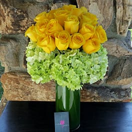 Yellow roses arranged with pale green hydrangeas in a tall green vase