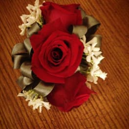 Red rose corsage with white flowers and ribbon on a wooden surface