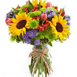 Bright mixed bouquet with sunflowers, purple daisies, and pink tulips in a glass vase