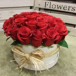 Red roses arranged in a white round box with a straw bow