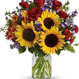 Bouquet of sunflowers, red roses, and mixed purple flowers in a glass vase