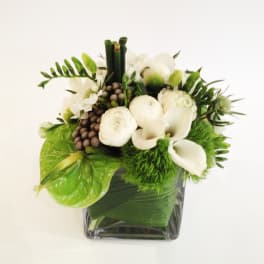 White flowers and green accents arranged in a square glass vase