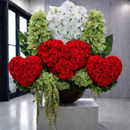 Heart-shaped red rose arrangement with white orchids and green flowers in a basket