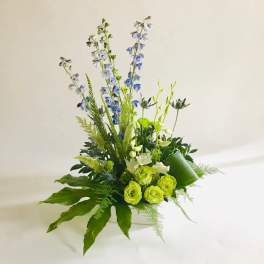 Tall green and blue floral arrangement in a white container