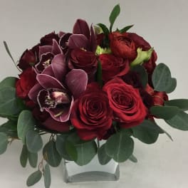 Red roses and purple orchids in a clear glass vase with eucalyptus