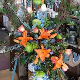 Tall floral wreath with orange lilies and mixed blooms on a stand