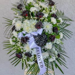Standing funeral wreath of white flowers and dark roses with a ribbon