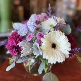 Bouquet of white and pink daisies with a butterfly accent in a glass vase