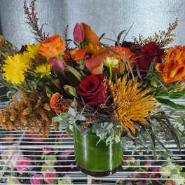 Mixed bouquet of red, orange, and yellow flowers in a green glass vase