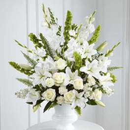 Tall all-white arrangement of lilies, roses, and carnations in a white urn-style vase