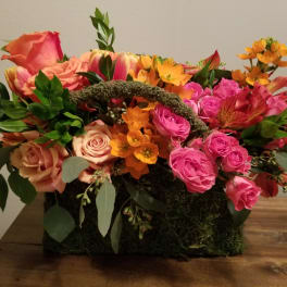 Mixed bouquet of pink and orange roses in a moss-covered basket