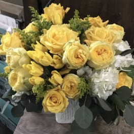 Yellow roses and tulips arranged in a white vase