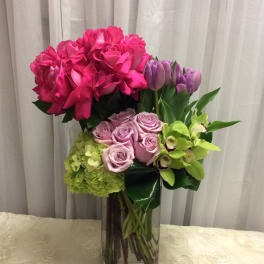Pink roses, lavender roses, tulips, hydrangea, and green orchids in a glass vase