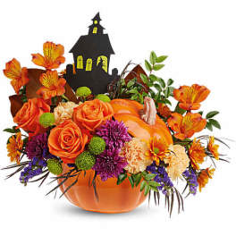 Orange floral arrangement in a pumpkin container with a haunted house pick