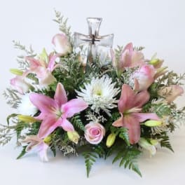 Pink lilies and white flowers arranged around a clear glass cross