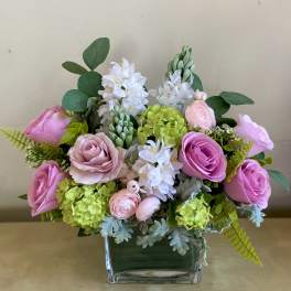 Low arrangement of pink roses, green hydrangeas, and white hyacinths in a clear glass rectangular vase