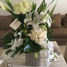 White roses, lilies, and orchids arranged in a square glass vase