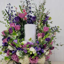 Large purple and pink floral arrangement around a white pillar candle