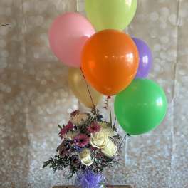 Bouquet of mixed flowers in a glass vase with colorful balloons