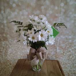 White daisy bouquet in a clear glass vase with a burlap bow