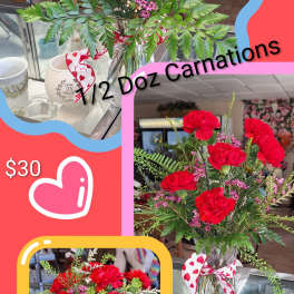 Red carnation bouquet in a glass vase with a heart ribbon