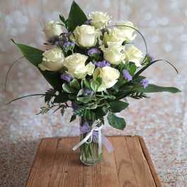 Bouquet of white roses and purple filler flowers in a glass vase