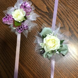 Two rose corsages with lavender ribbons on a wooden surface