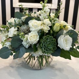 White roses and greenery arranged in a clear glass vase with succulents.
