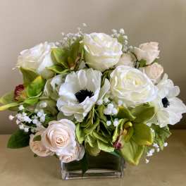 Low arrangement of white and blush roses with white anemones and green orchids in a clear glass vase.