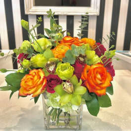 Bright mixed bouquet of roses and green orchids in a clear glass vase