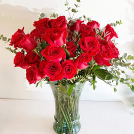 Red roses arranged in a clear glass vase with airy greenery