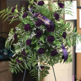 Standing floral spray with purple carnations and a purple ribbon