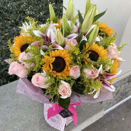 Bouquet of sunflowers, pink roses, and lilies wrapped in pink paper